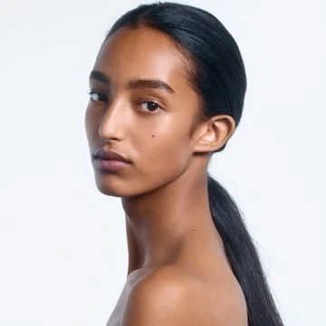 Close-up portrait of an adult woman with dark hair pulled back in a ponytail, gazing intently at the camera against a white background.