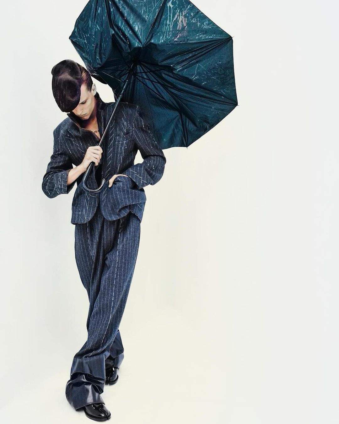 Full shot of person in striped suit holding umbrella against a white backdrop, creating a stylish and eye-catching fashion photograph.