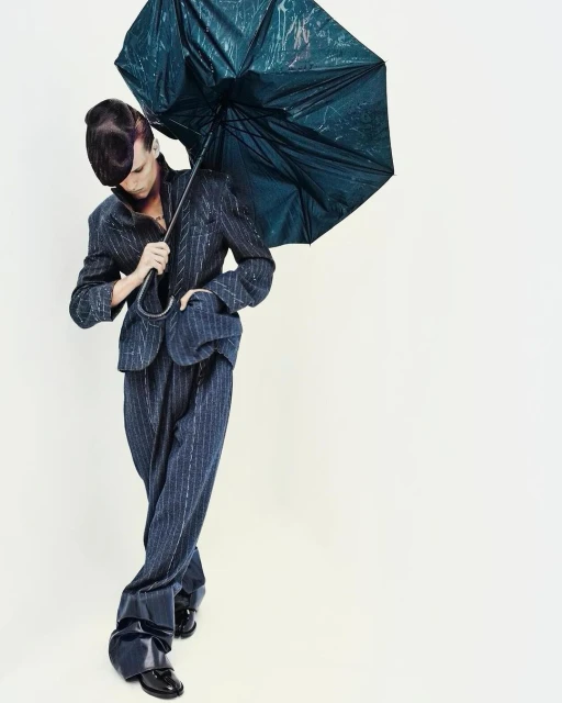 Full shot of person in striped suit holding umbrella against a white backdrop, creating a stylish and eye-catching fashion photograph.
