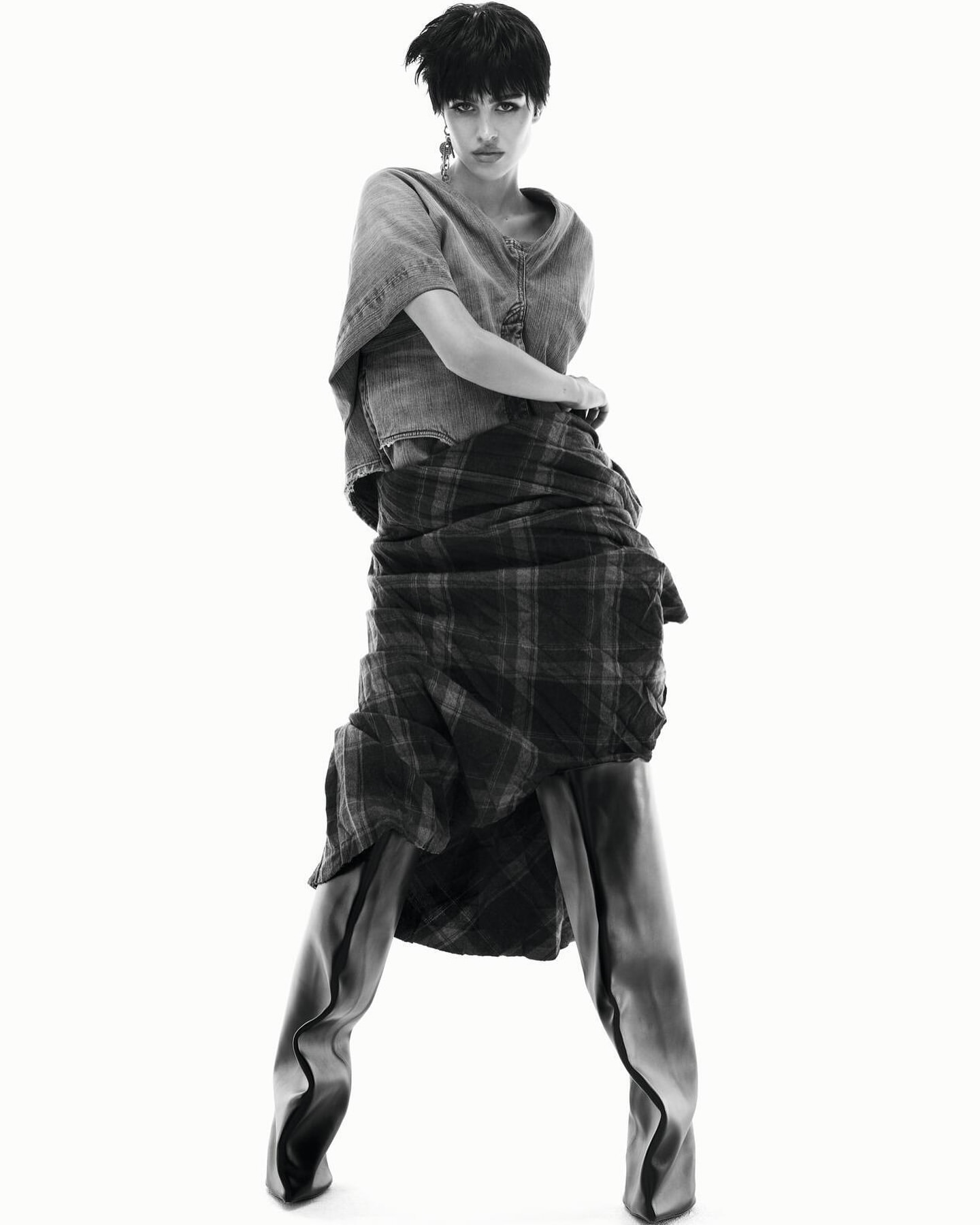 Monochrome fashion shot of a woman in an unconventional layered outfit posing against a white backdrop in a studio setting.