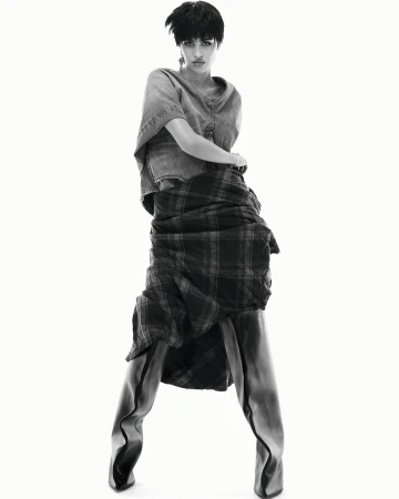 Monochrome fashion shot of a woman in an unconventional layered outfit posing against a white backdrop in a studio setting.