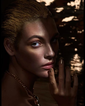 Close-up portrait of a woman with metallic gold hair, shimmering skin highlights, and a gold chain necklace by photographer Solve Sundsbo.