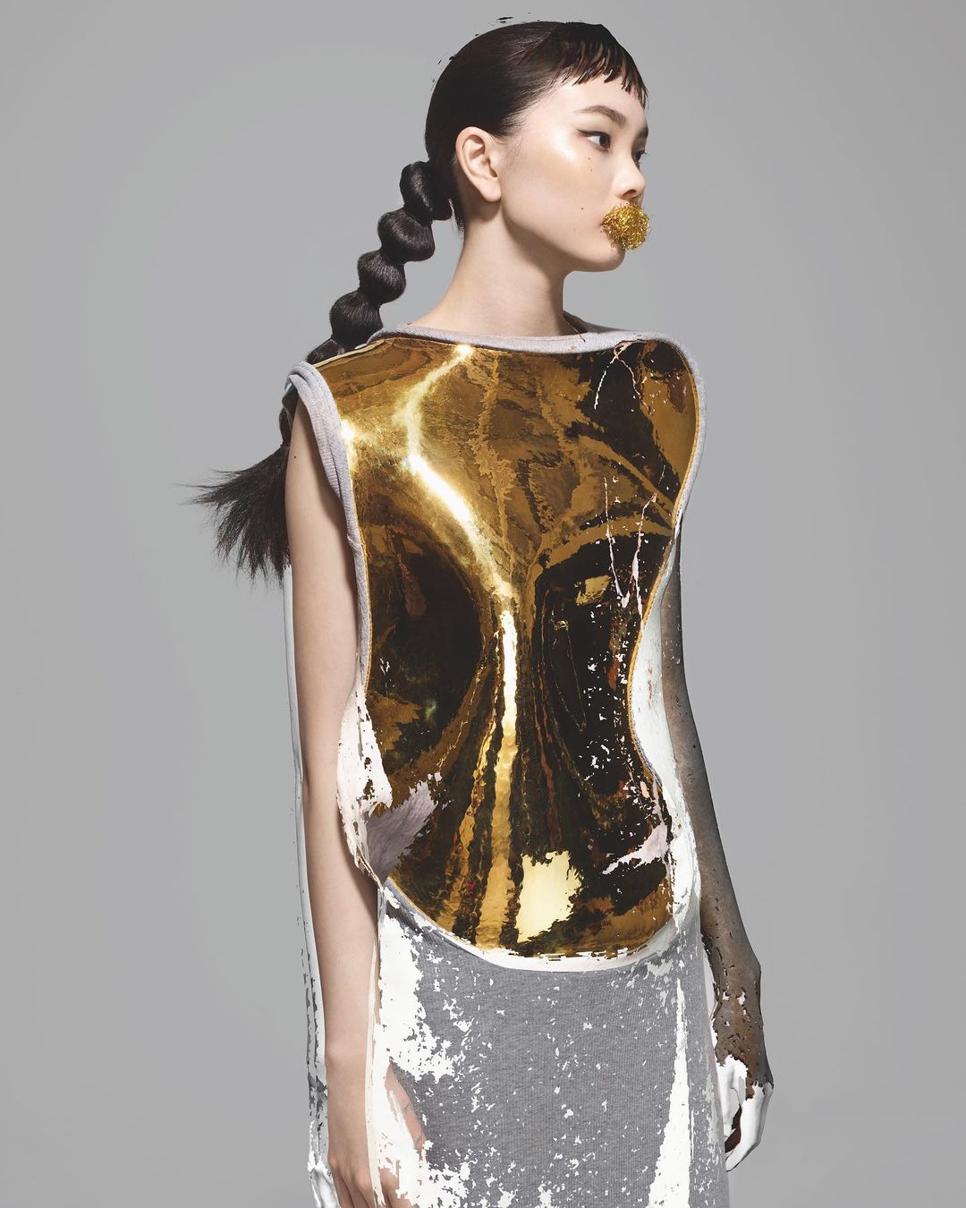 High fashion portrait of a young Asian woman in an abstract gold and white dress with an avant-garde braided hairstyle in a studio.