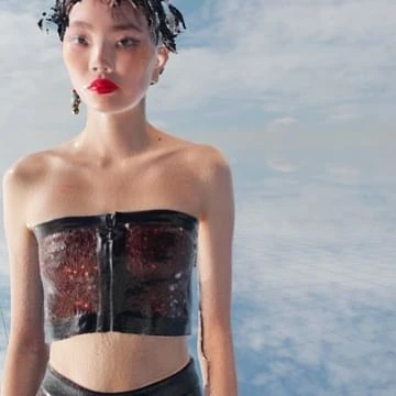 Portrait of an East Asian model wearing a strapless dark top against a sky and cloud background by photographer Solve Sundsbo.