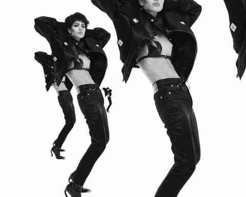 Three fashion models in black jackets, bra tops, and denim, striking poses against a stark white backdrop in a studio shot.