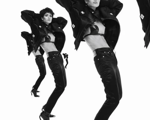 Three fashion models in black jackets, bra tops, and denim, striking poses against a stark white backdrop in a studio shot.