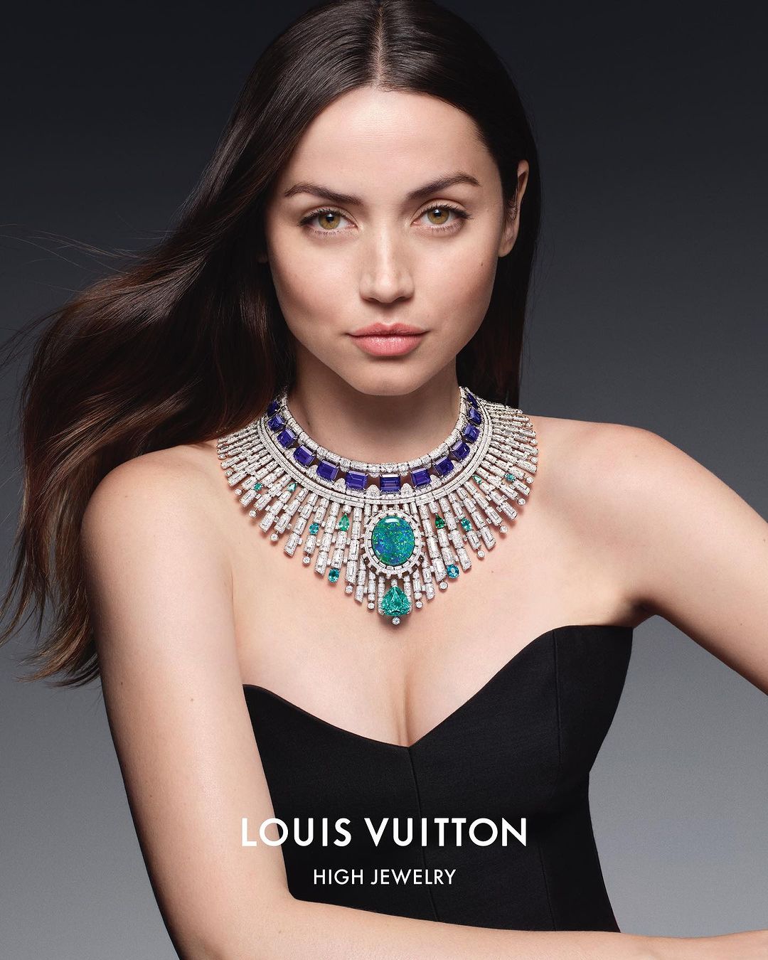 Portrait of a brunette woman wearing a black dress and an elaborate, multi-colored gemstone statement necklace for Louis Vuitton High Jewelry.