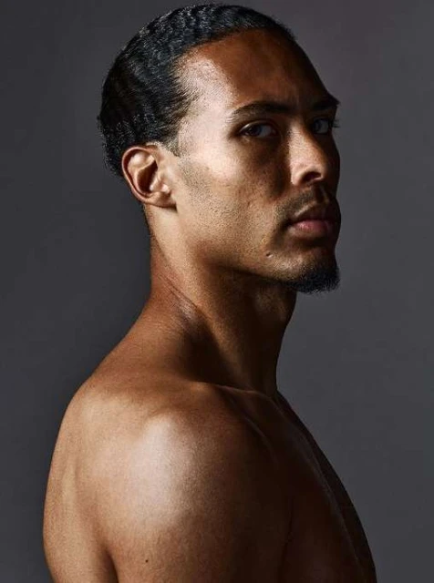 Portrait of a shirtless adult male with dark hair in a photo studio with even lighting and a dark gray background. High-key lighting.