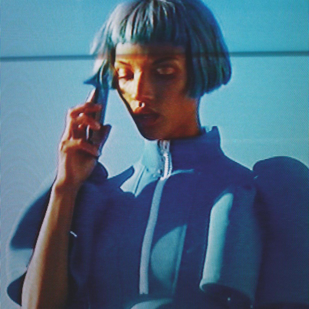 Woman with blue hair and a futuristic outfit stands in front of a blue wall. Fashion forward portrait with unique style.