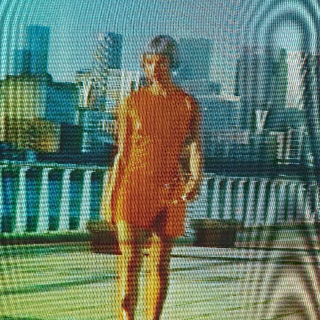 Woman in an orange dress walking along a waterfront pier with city skyline in background