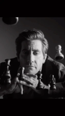 Black and white portrait of an adult male actor gazing forward surrounded by floating chess pieces in an indoor studio environment.