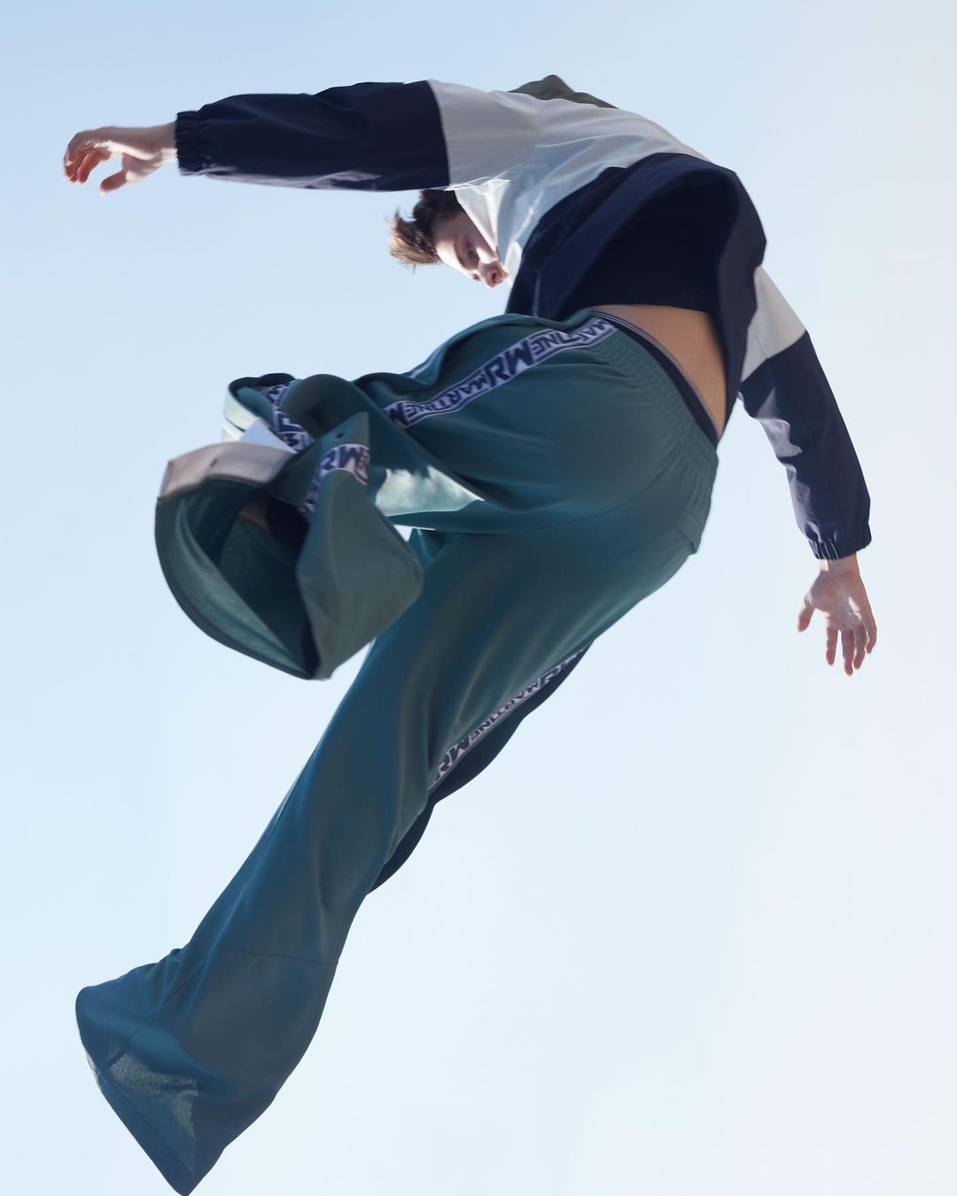A person in sportswear poses dynamically against a bright blue sky, capturing a moment of movement and style in an outdoor setting.