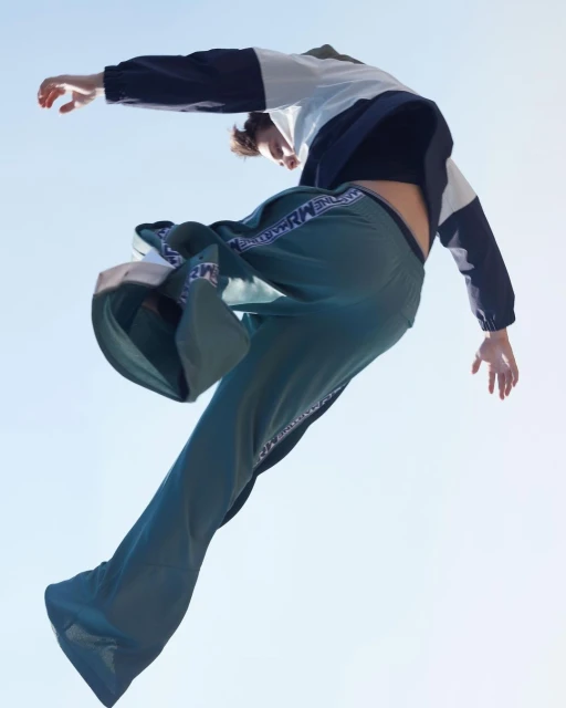 A person in sportswear poses dynamically against a bright blue sky, capturing a moment of movement and style in an outdoor setting.