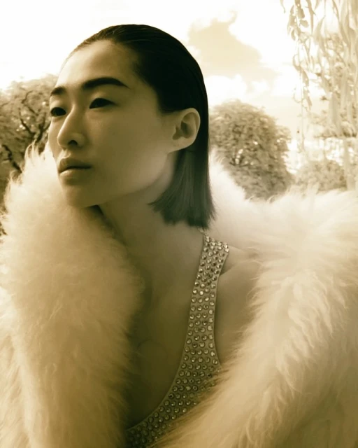 Portrait of a stylish adult female with an Asian appearance wearing an embellished sleeveless top and a white faux fur coat outdoors.