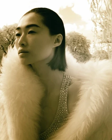 Portrait of a stylish adult female with an Asian appearance wearing an embellished sleeveless top and a white faux fur coat outdoors.