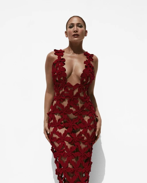 Jennifer Lopez poses in a form-fitting red floral dress against a bright white backdrop, creating a striking visual contrast in a fashion portrait.