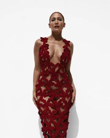 Jennifer Lopez poses in a form-fitting red floral dress against a bright white backdrop, creating a striking visual contrast in a fashion portrait.