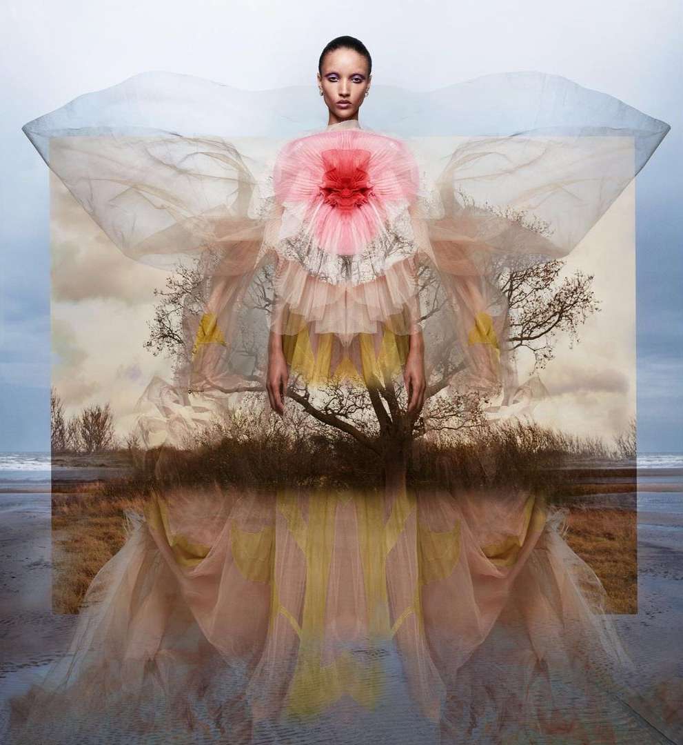Elegant woman in a flowing pink and yellow gown, standing against a beach landscape, creating a surreal fashion portrait with soft lighting.