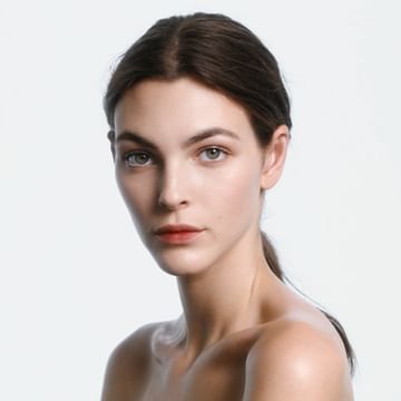 Close-up portrait of a young, fair-skinned woman with brown hair pulled back, nude shoulders, and a neutral expression against a light backdrop.