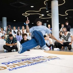 Dancer in motion mid-air over a branded floor during a breakdancing event captured by Sophie Brandstrom in Paris.