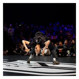 Breakdancer performing a freeze upside down on a stage before an audience, photographed by Sophie Brandstrom in Paris.