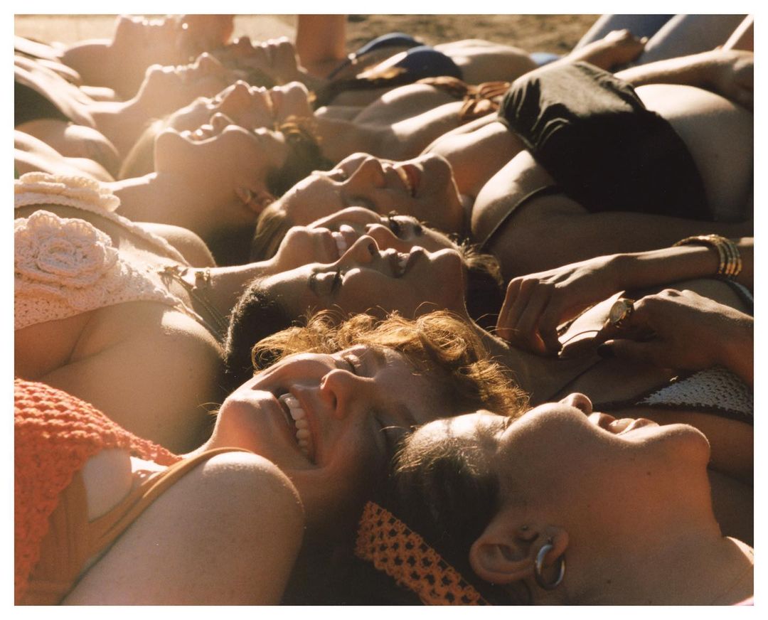 A group of young adult women lies on a sunny beach, wearing swimsuits, bikinis, and jewelry in this eye-level summertime shot. 