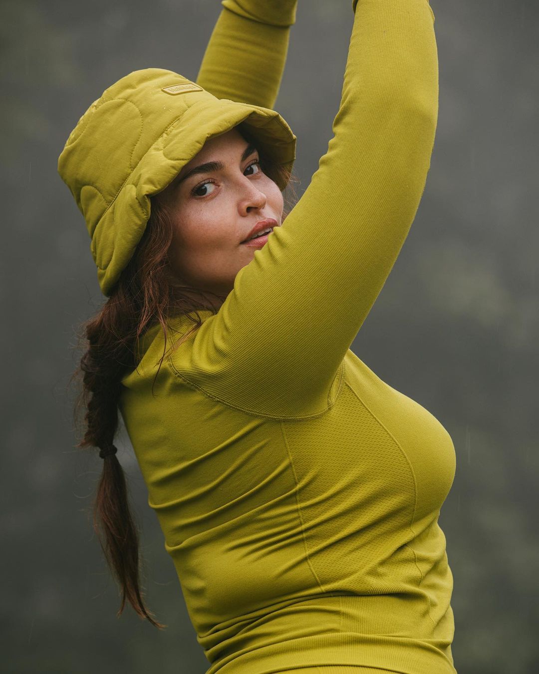 Woman in a chartreuse long-sleeved shirt and padded bucket hat poses in a misty outdoor setting, creating a soft and natural portrait.