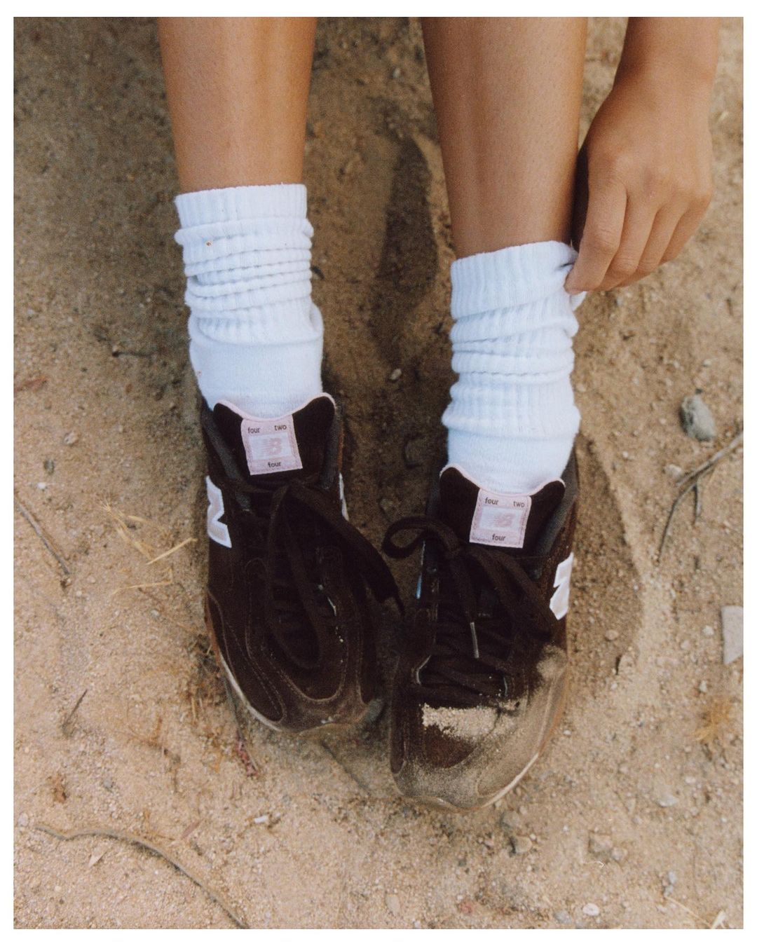 Eye-level shot of feet in athletic shoes, and white socks on a sandy surface, one hand pulls the sock up.