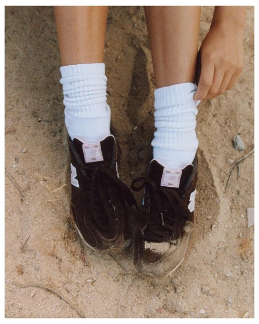 Eye-level shot of feet in athletic shoes, and white socks on a sandy surface, one hand pulls the sock up.