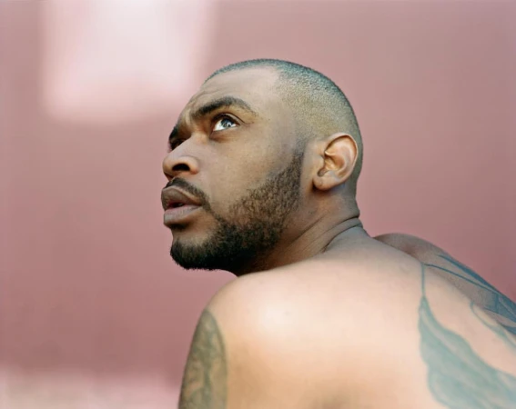 Low angle portrait of a Black adult male looking up and away from the camera, visible tattoos on the shoulder and arm.