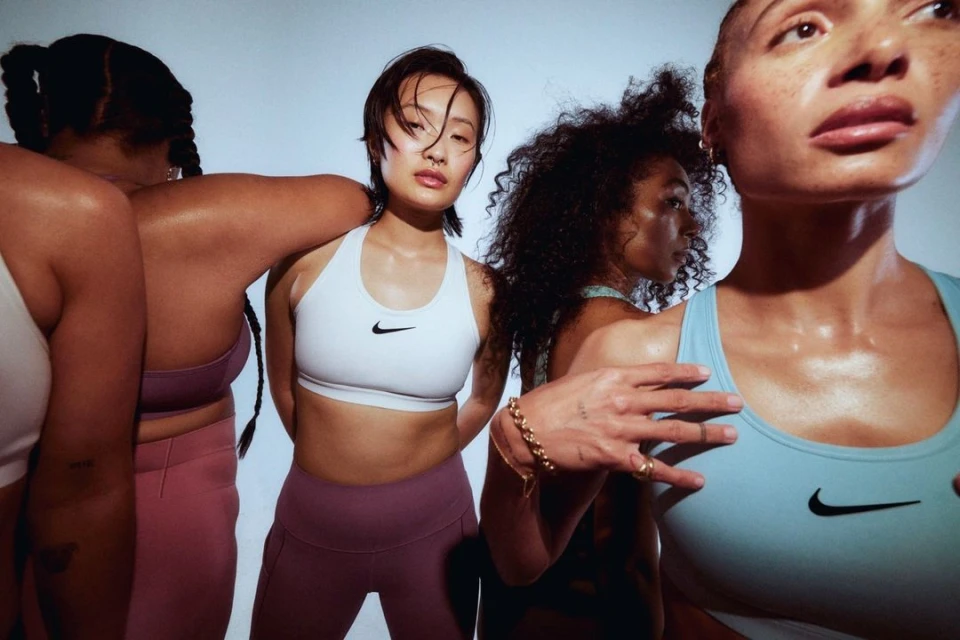Group of diverse women in sports bras and leggings posing in a studio setting against a soft, gradient background. Fitness and activewear promotion.