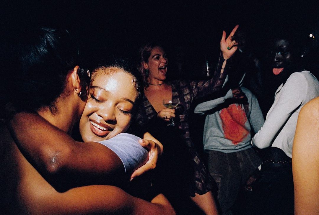 A group of young adults are enjoying a celebration indoors at nighttime, with smiling faces and a joyful, lively atmosphere and dark lighting.