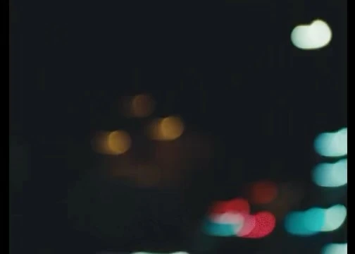 Blurred image of colorful bokeh lights at night, including blue, white, red, and orange.