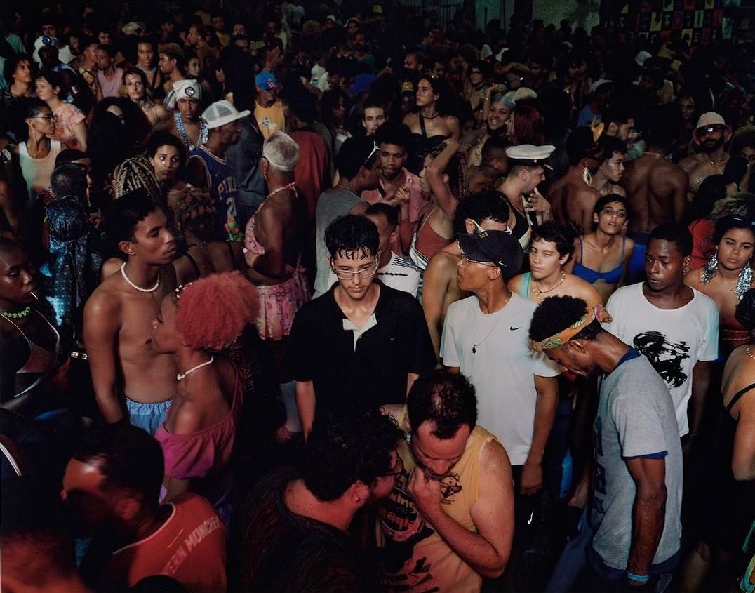 Large diverse crowd gathers at night. Adults are seen socializing, dancing, and interacting at an indoor event with dark lighting.