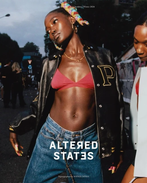 Two women model in a fashion editorial. One woman in a red bra top, jeans, and jacket is in focus in an urban outdoor setting.
