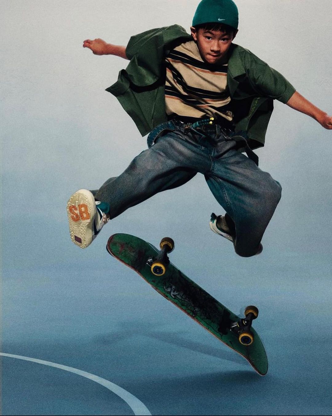 Young adult male skateboarder in mid-air with skateboard performing trick in blue and white indoor skate park setting, wearing casual clothing.