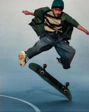 Young adult male skateboarder in mid-air with skateboard performing trick in blue and white indoor skate park setting, wearing casual clothing.