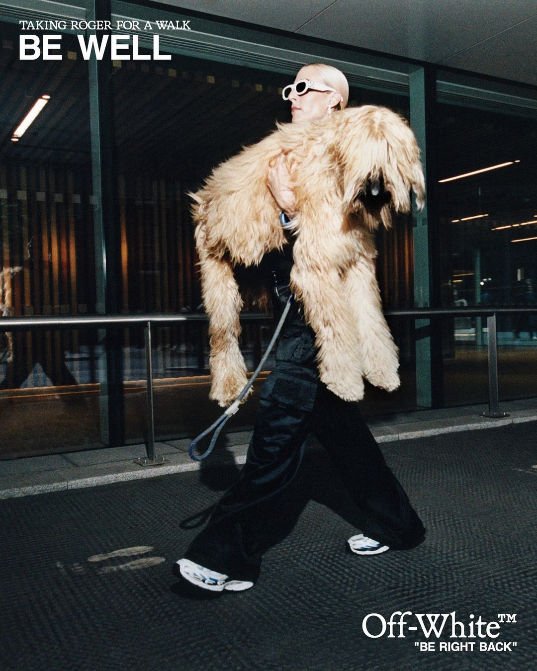 Adult carries a furry dog-like garment over shoulder in urban setting. Person with sunglasses walks on patterned pavement at night.
