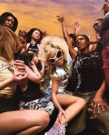 Group of people posing in an outdoor setting with a warm, colorful sky, including adult women with diverse hairstyles and fashion styles.