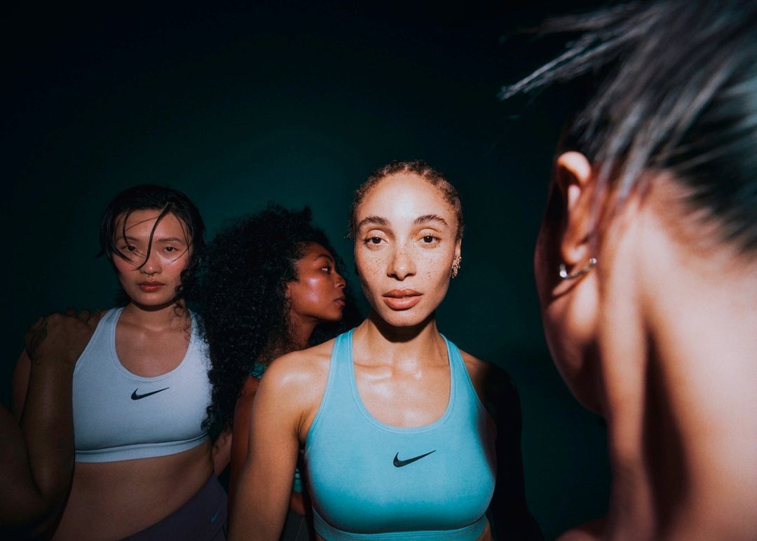 Four women in athletic wear pose in front of a dark teal background, showcasing fashion, fitness, and diverse representation.