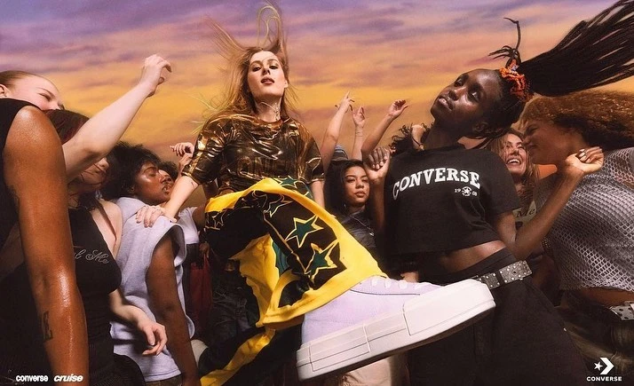 Promotional shot with a group of diverse young adult women, a Converse sneaker, and the Converse logo against a colourful gradient background.
