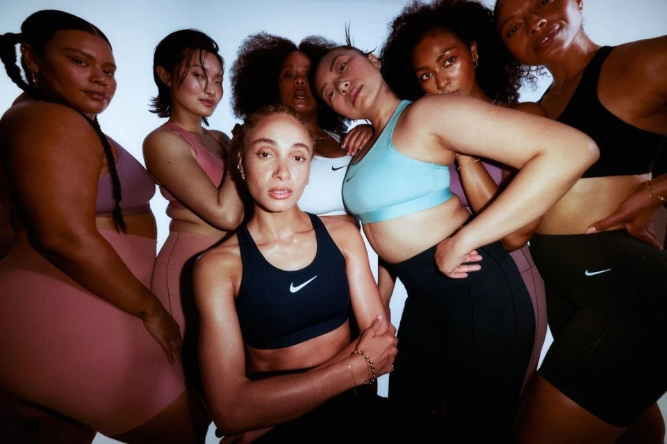 Group of six diverse women in sports bras and athletic wear, posing in a photo studio against a bright white background for a fitness advertisement.
