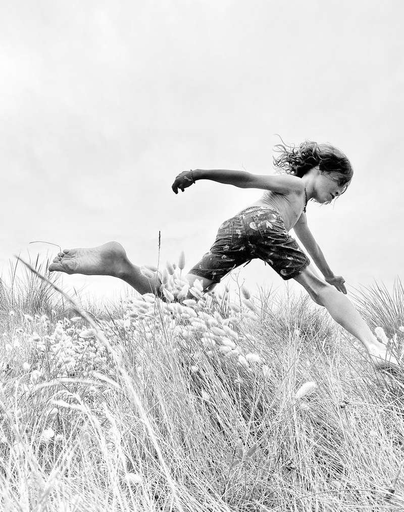 Young boy leaping through tall grass in a black and white outdoor scene, capturing a moment of playful energy and freedom in nature.