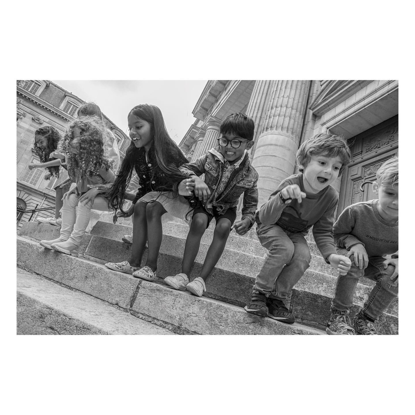 Black and white image of group of children of mixed ethnicities sitting on stone steps of building with large columns.