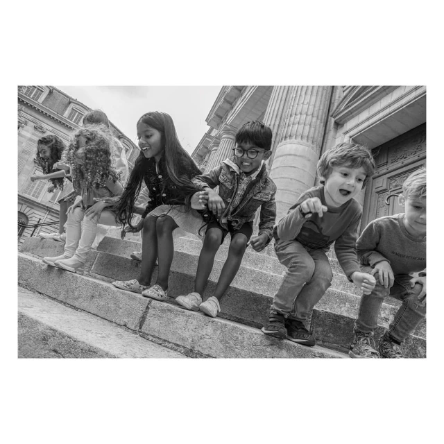 Black and white image of group of children of mixed ethnicities sitting on stone steps of building with large columns.
