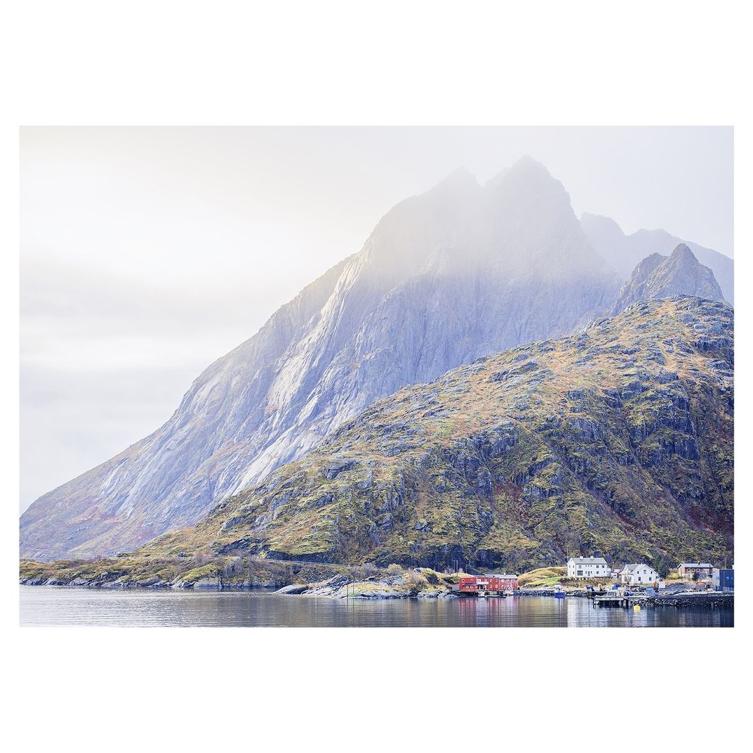 Scenic landscape of mountains meeting water in Norway, with fog and a small village in the foreground on a cloudy day.