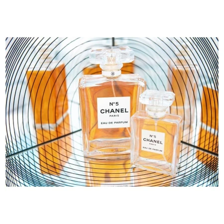 Close-up studio shot of two Chanel No. 5 perfume bottles of different sizes, set against a reflected amber and spiral background.