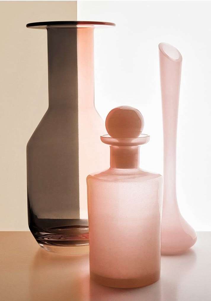 Elegant still life composition of three glass vases in varying shapes and shades of pink and brown, set against a two-tone background.
