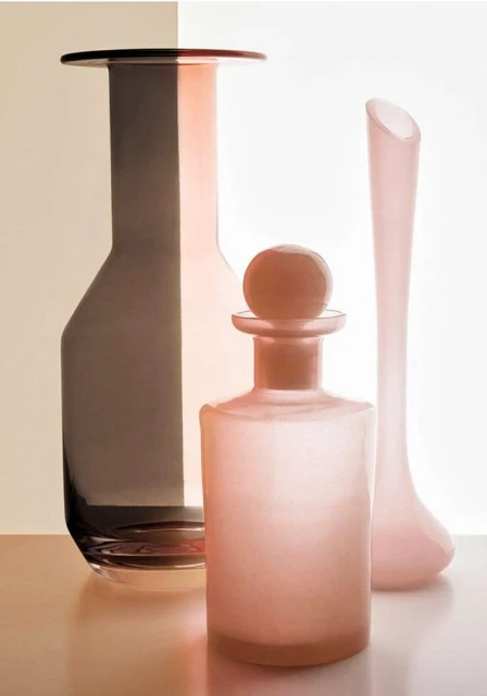 Elegant still life composition of three glass vases in varying shapes and shades of pink and brown, set against a two-tone background.