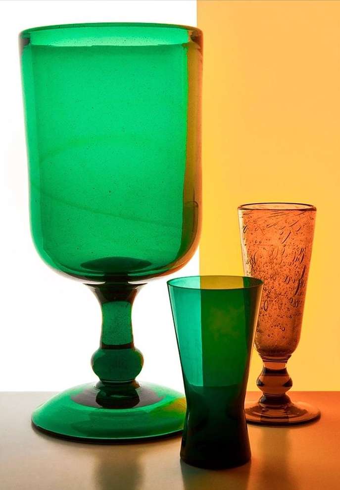 A still life featuring three glasses of different sizes and colors arranged against a split yellow and white background.